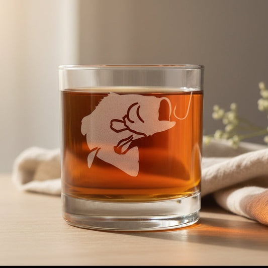 A clear rocks glass with a bass fish silhouette etched on the front, filled with a dark red liquid, set against a neutral background