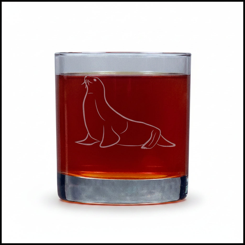 A clear rocks glass with an etched seal design, filled with an amber-red liquid, set against a white background.