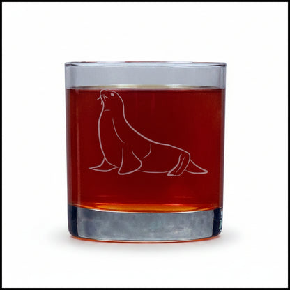A clear rocks glass with an etched seal design, filled with an amber-red liquid, set against a white background.
