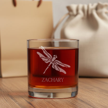 A clear rocks glass filled with amber-red liquid, featuring an etched dragonfly design and the name 'ZACHARY' on the front.