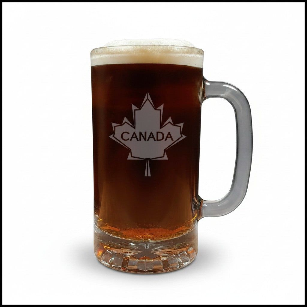 A clear glass beer mug filled with dark amber beer, topped with white foam, featuring a white maple leaf design with the word CANADA on the front, set against a plain white background.