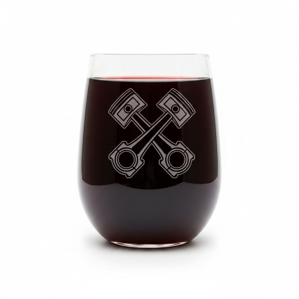 A clear stemless wine glass filled with dark red wine, featuring an etched crossed-piston engine design on the front, set against a plain white background.
