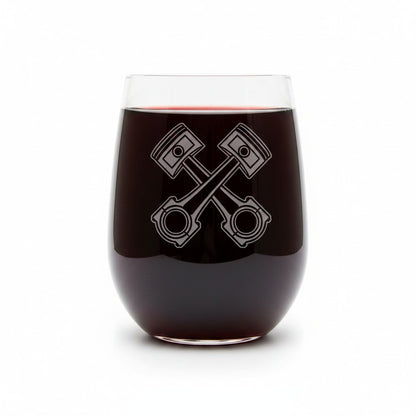 A clear stemless wine glass filled with dark red wine, featuring an etched crossed-piston engine design on the front, set against a plain white background.