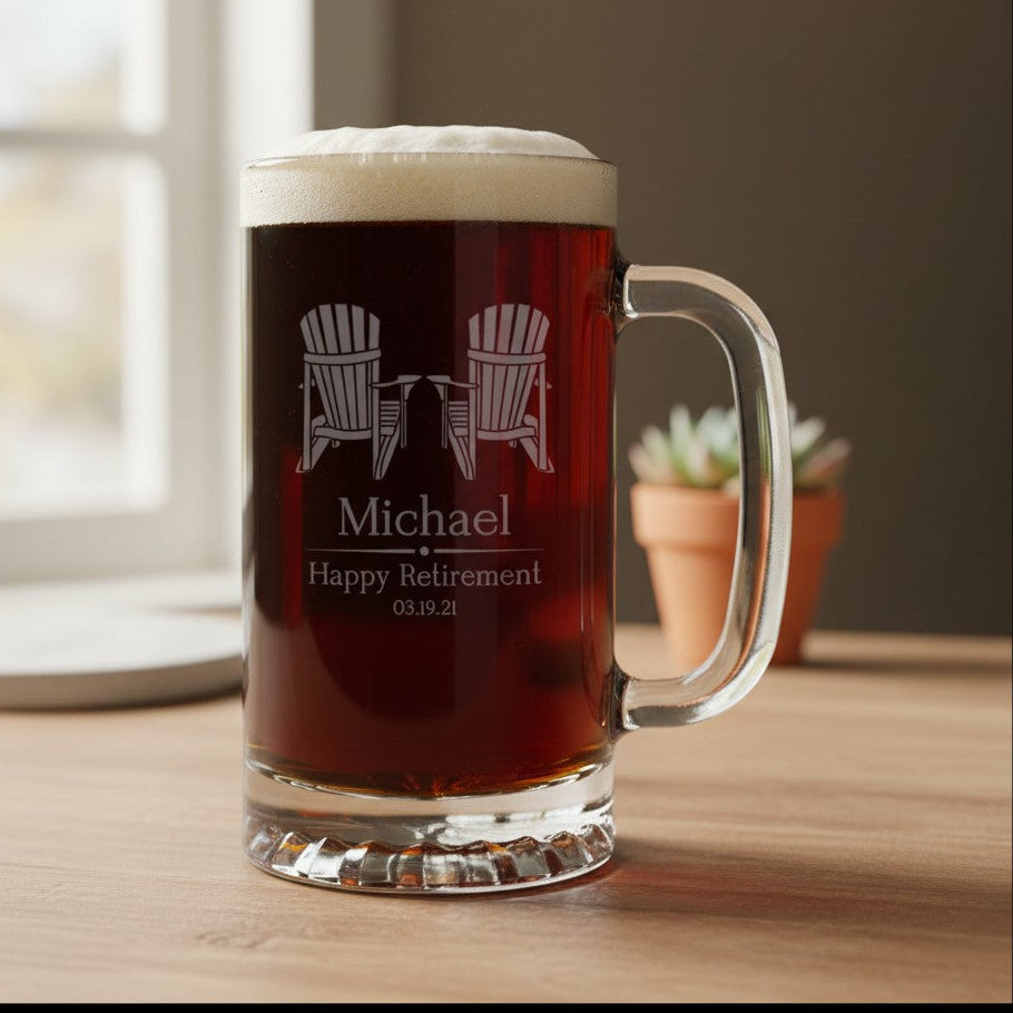 A clear glass beer mug filled with dark beer and foam, standing on a wooden table near a window, with etched Adirondack chairs. The mug is personalized with etched text reading 'Michael Happy Retirement 03.