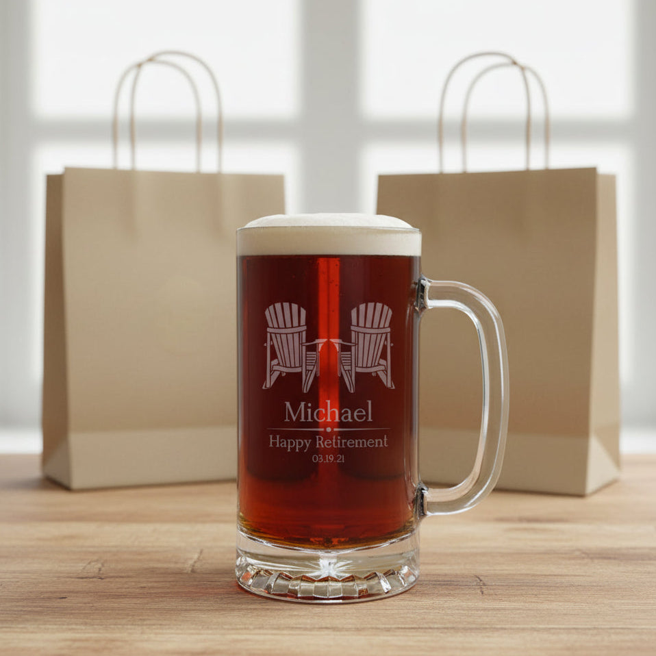 A clear glass beer stein mug filled with dark beer, standing on a light wood surface against a black background. The mug is etched with two Adirondack chairs, the name Michael, and the text Happy Retirement with a date.