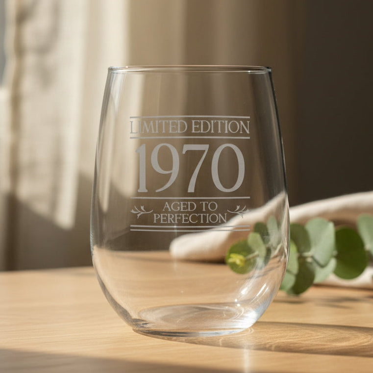 A clear stemless wine glass with etched silver text reading 'LIMITED EDITION 1970 AGED TO PERFECTION', shown on a wooden surface 