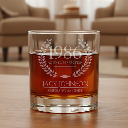 Glass tumbler with engraved text '1986 Aged to Perfection, Jack Johnson Cheers to 40 Years' on a gray background.