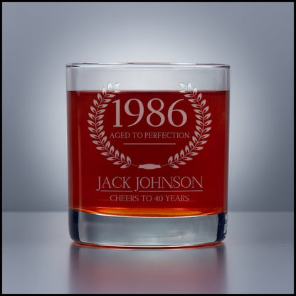 Glass tumbler with engraved text '1986 Aged to Perfection, Jack Johnson Cheers to 40 Years' on a gray background.