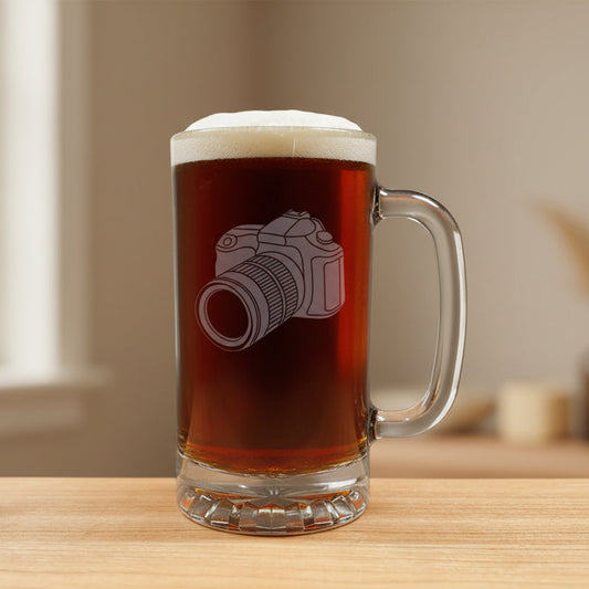 A clear glass beer mug filled with dark beer, featuring an etched camera design on the front, set on a light wood 