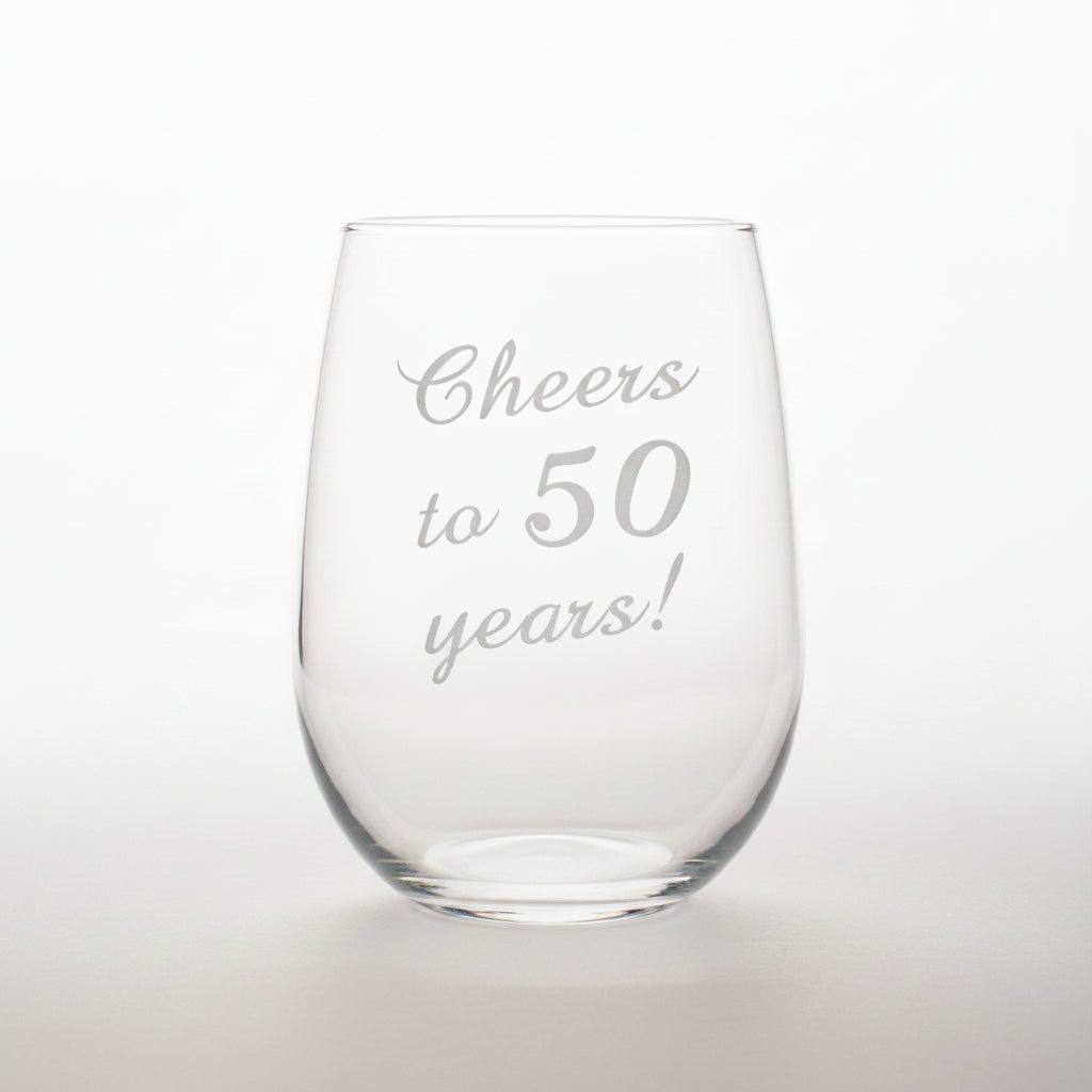 Clear glass stemless wine glass with 'Cheers to 50 years!' engraving on a black background.