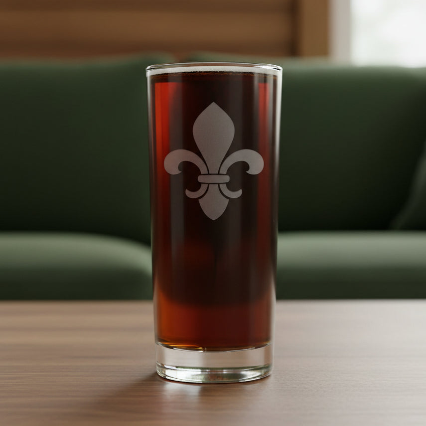 A clear pint glass filled with dark beer, featuring a white fleur-de-lis emblem on the front, set against a textured gray background.