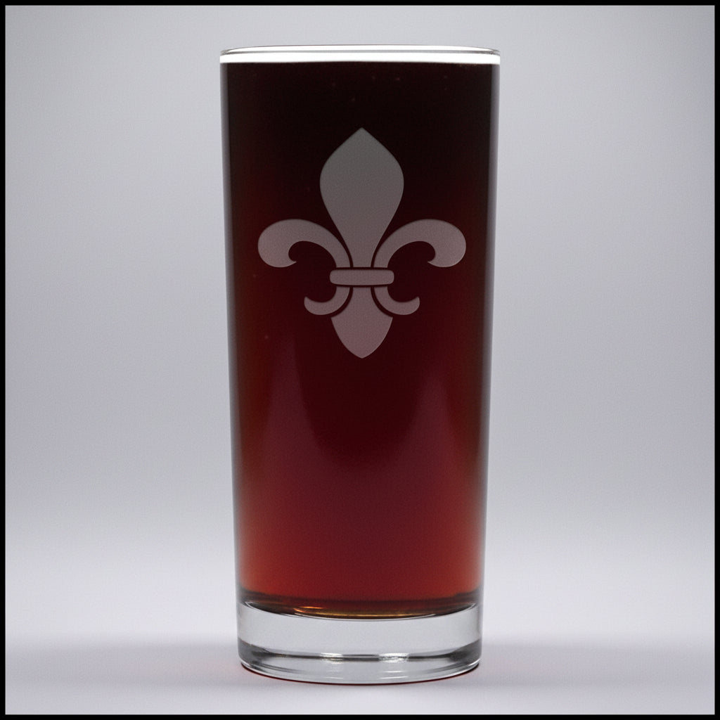 A clear pint glass filled with dark beer, featuring a white fleur-de-lis emblem on the front, set against a little gray background.