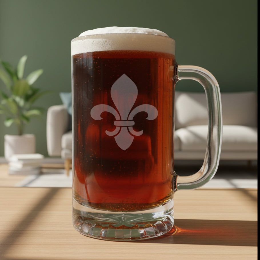 A clear glass beer mug with a handle, filled with dark brown beer and topped with white foam, featuring a white fleur-de-lis symbol on the front. The mug is placed on a light wood surface against a living room background.