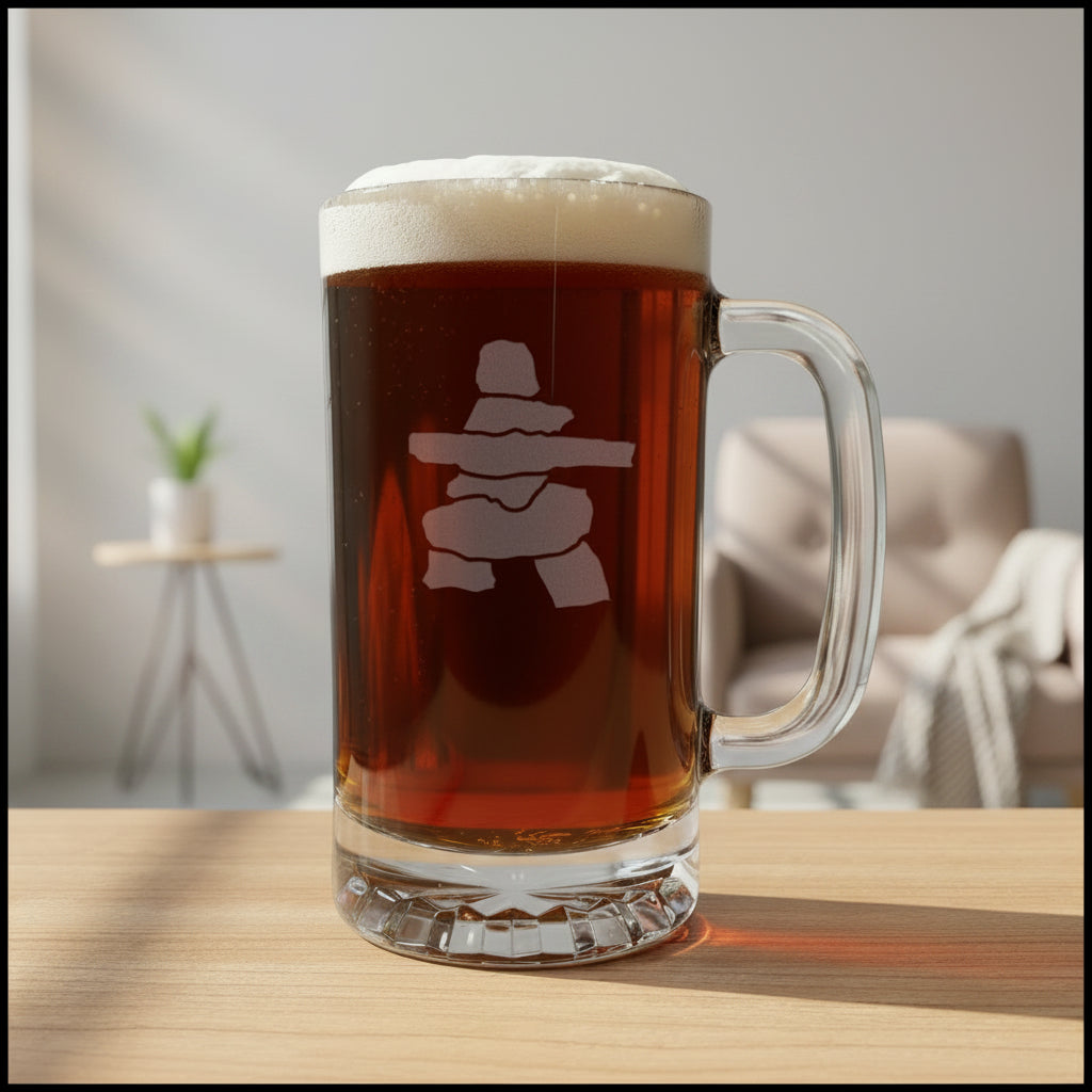 A clear glass beer mug filled with dark amber beer and topped with white foam, featuring a Inuksuk design on the front, set on a light wood surface 
