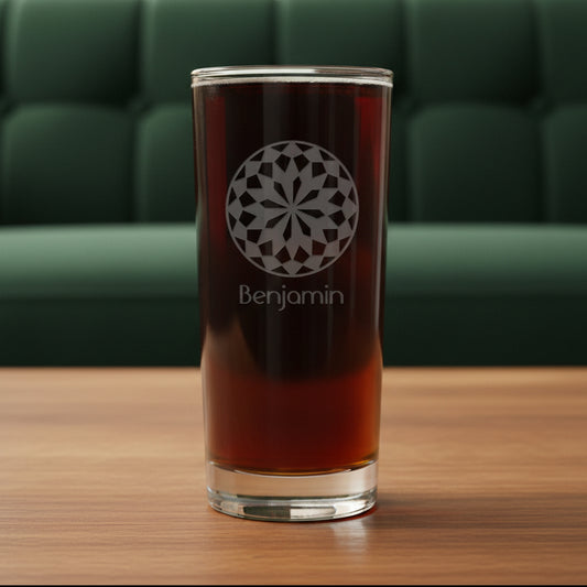 A clear highball glass filled with a dark red-brown beverage, featuring an etched white geometric circular design and the name 'Benjamin' on the front, set against a textured gray background.