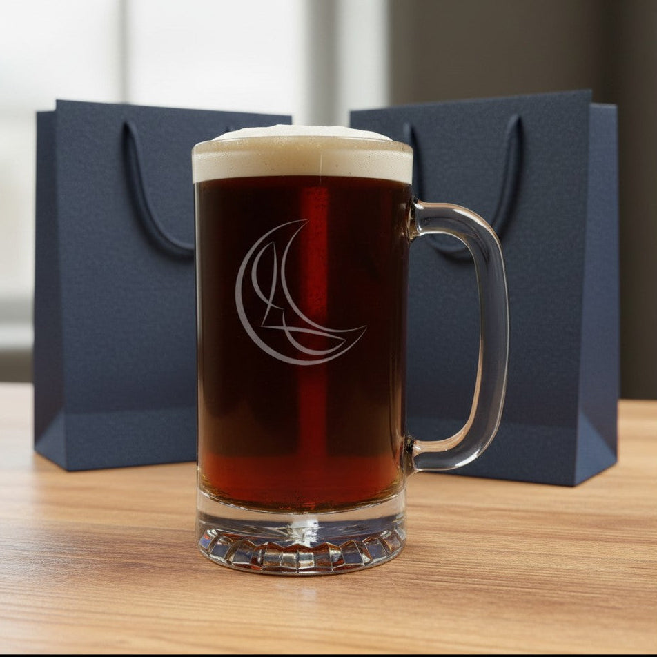 A clear glass beer mug filled with dark beer and topped with white foam, standing on a wooden table. The mug has a an etched crescent moon design.
