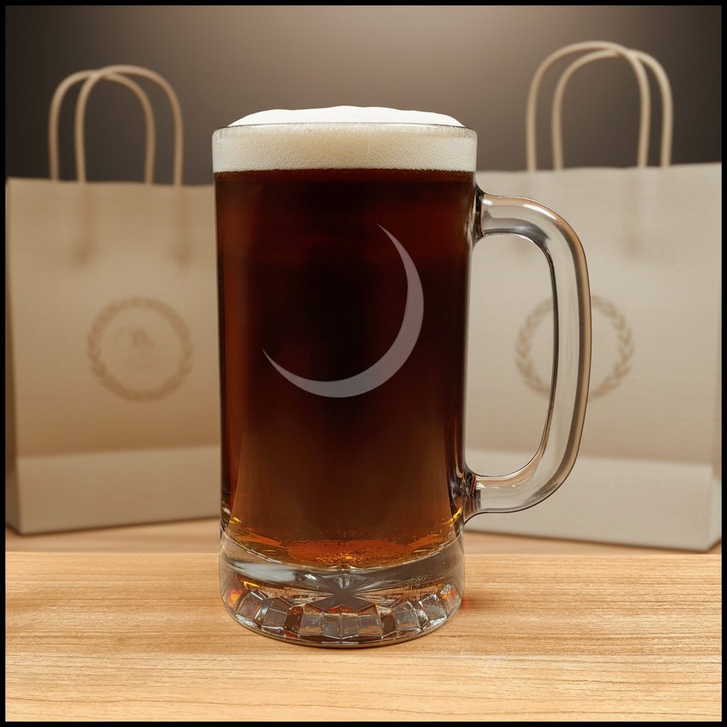 A clear glass beer mug with a handle, filled with dark beer and topped with white foam, featuring an etched crescent moon graphic on the front,