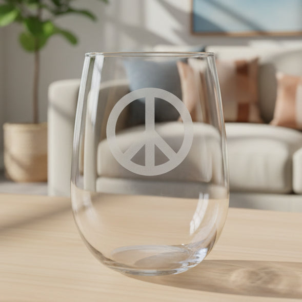 A clear stemless wine glass with a gray peace sign etched on the front, resting on a wooden surface bright living room background.