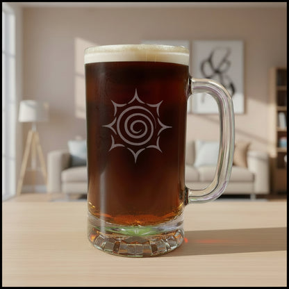 A clear glass beer mug with a handle, filled with dark amber beer and topped with white foam, featuring a etched spiral sunburst design on the front, set on a light wood surface against a black background.