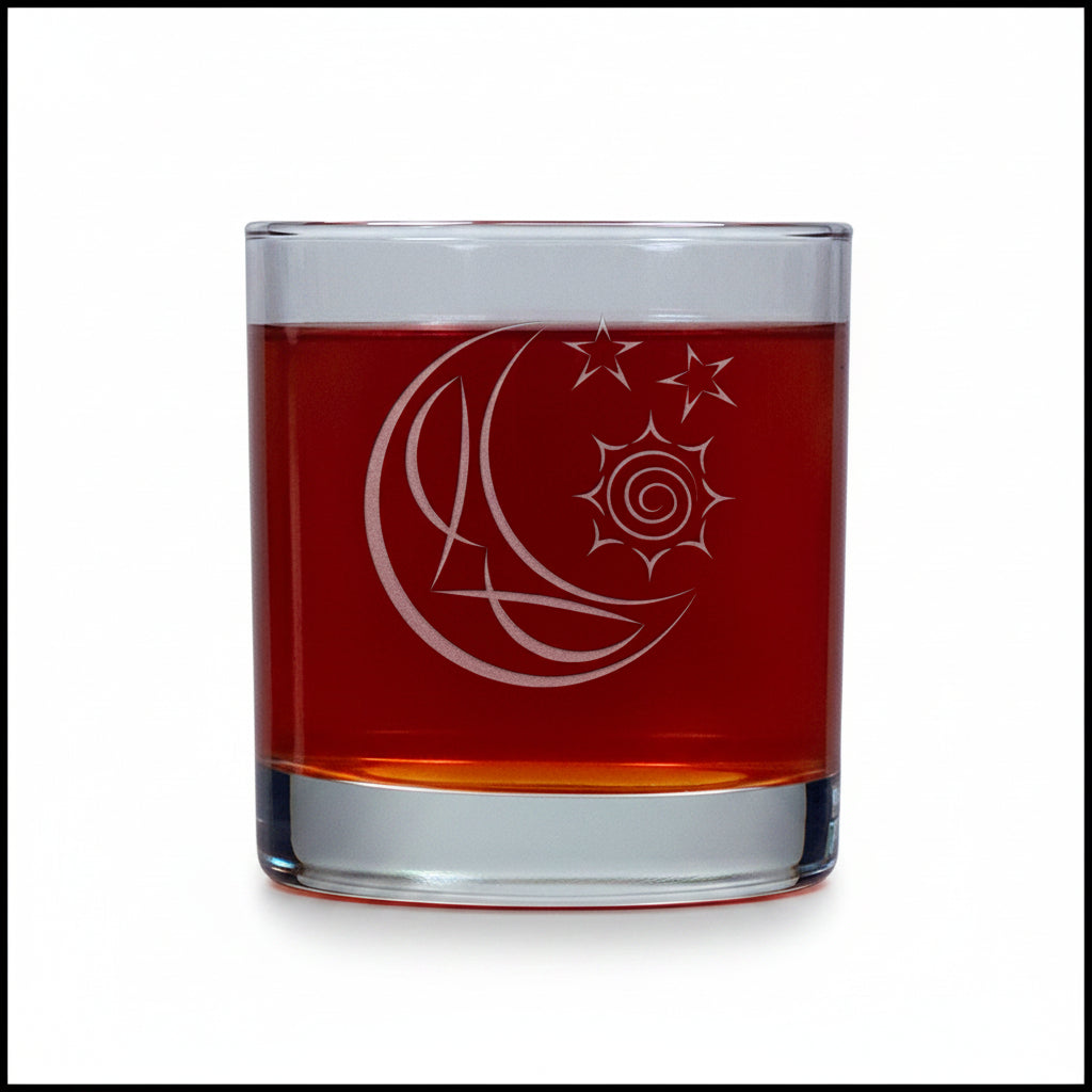 A clear glass rocks tumbler filled with an amber-brown liquid, featuring an etched crescent moon and star design on the front, set against a textured white background.
