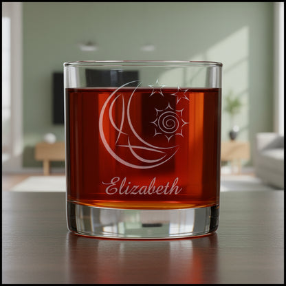 A clear glass rocks tumbler with an etched crescent moon and star design, filled with a dark red liquid, shown against a living room.