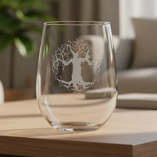 A clear stemless wine glass with a silver etched tree of life design, resting on a wooden surface against Living room