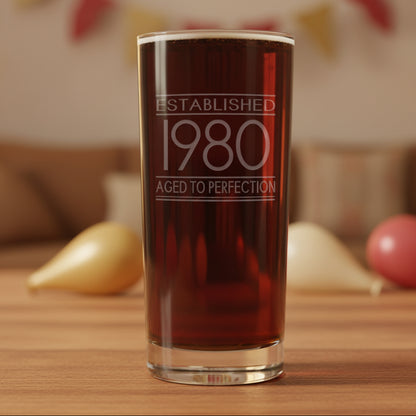 Glass with 'Established 1980 Aged to Perfection' text with ballons n the background