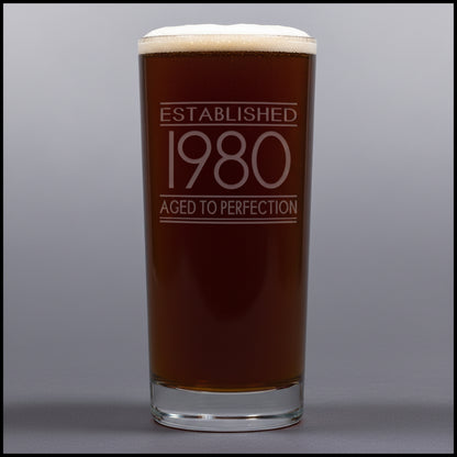 Glass with 'Established 1980 Aged to Perfection' text on a gray background