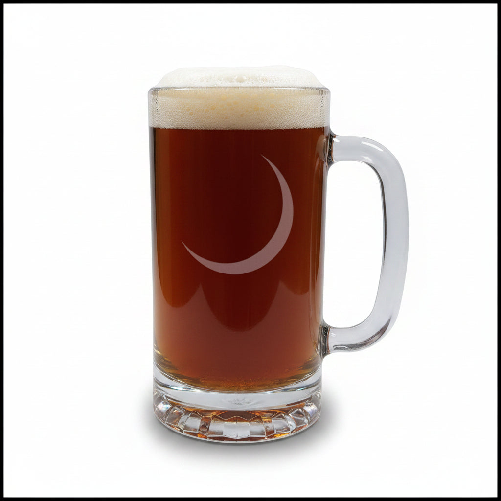 A clear glass beer mug with a handle, filled with dark beer and topped with white foam, featuring a etched crescent moon on the front, set on a wooden surface against a black background.