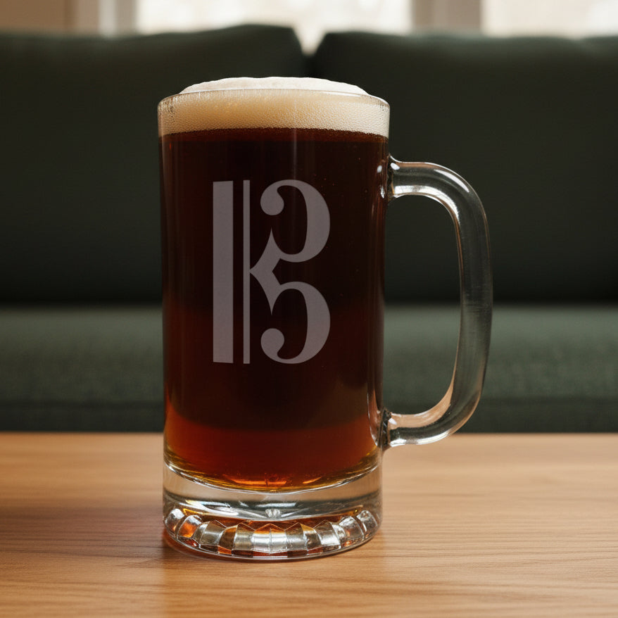 Glass mug with a alto clef engraving filled with dark beer on a wooden surface with a green couch in the background