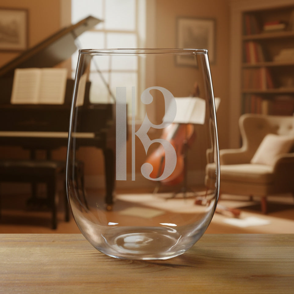 Stemless wine glass with a alto clef etching on a wooden surface with a music room in the background