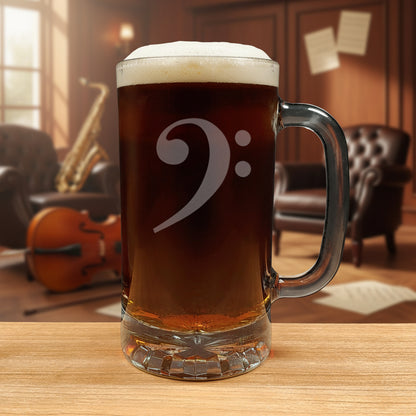 Glass mug with a bass clef engraving filled with dark beer on a wooden surface with a music room in the background