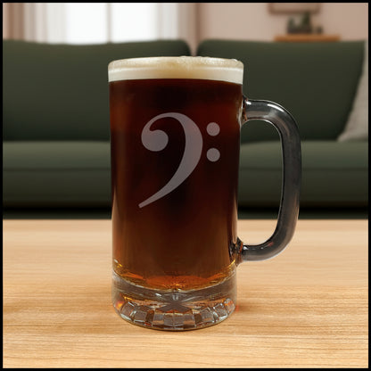 Glass mug with a bass clef engraving filled with dark beer on a wooden surface with a green couch in the background