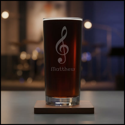Cooler glass with a treble clef engraving filled with dark beer on a wooden surface with a music room in the background