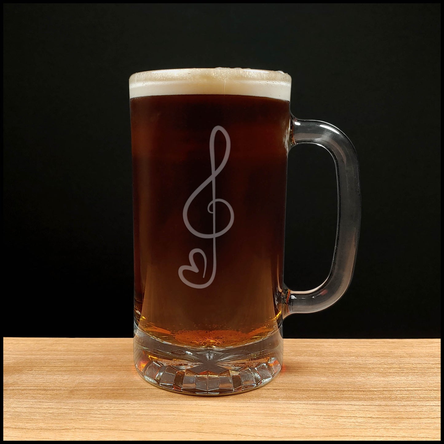 Glass mug with a treble clef with heart "tail" engraving filled with dark beer on a wooden surface 