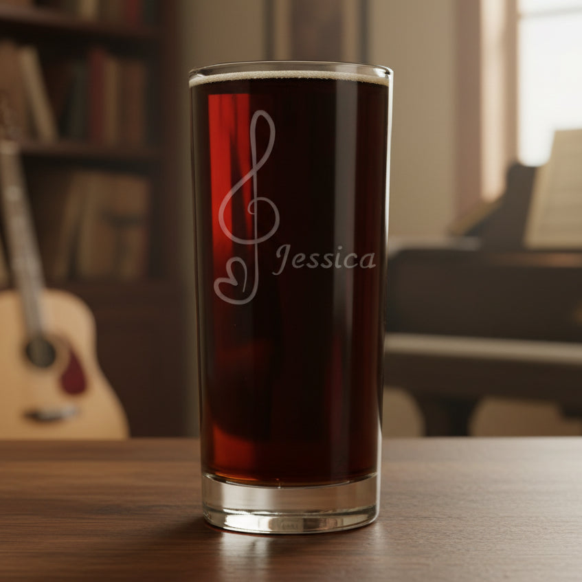 Cooler glass with a treble clef with heart "tail"engraving filled with dark beer on a wooden surface with a music room in the background