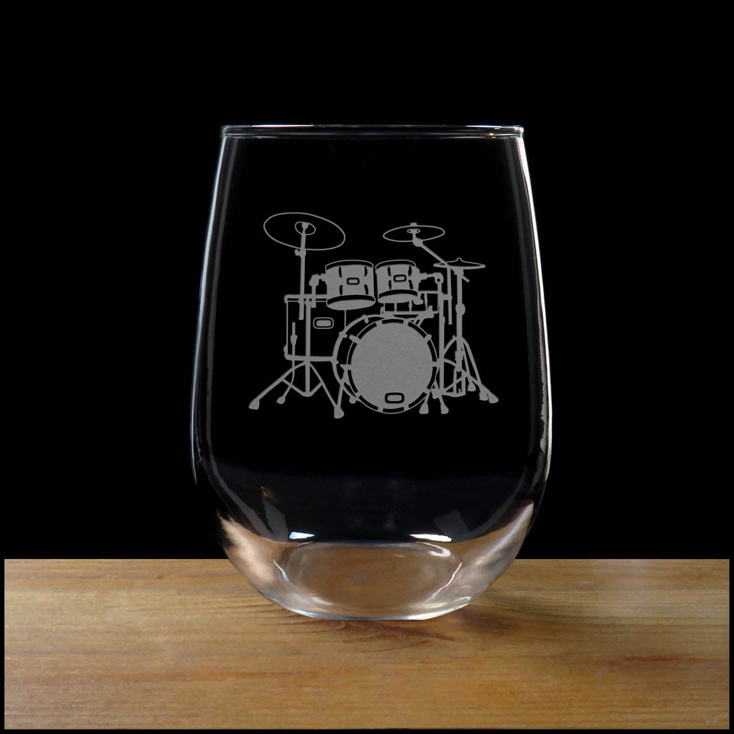 Stemless wine glass with etched Drum Set Design on a wood surface with a black background