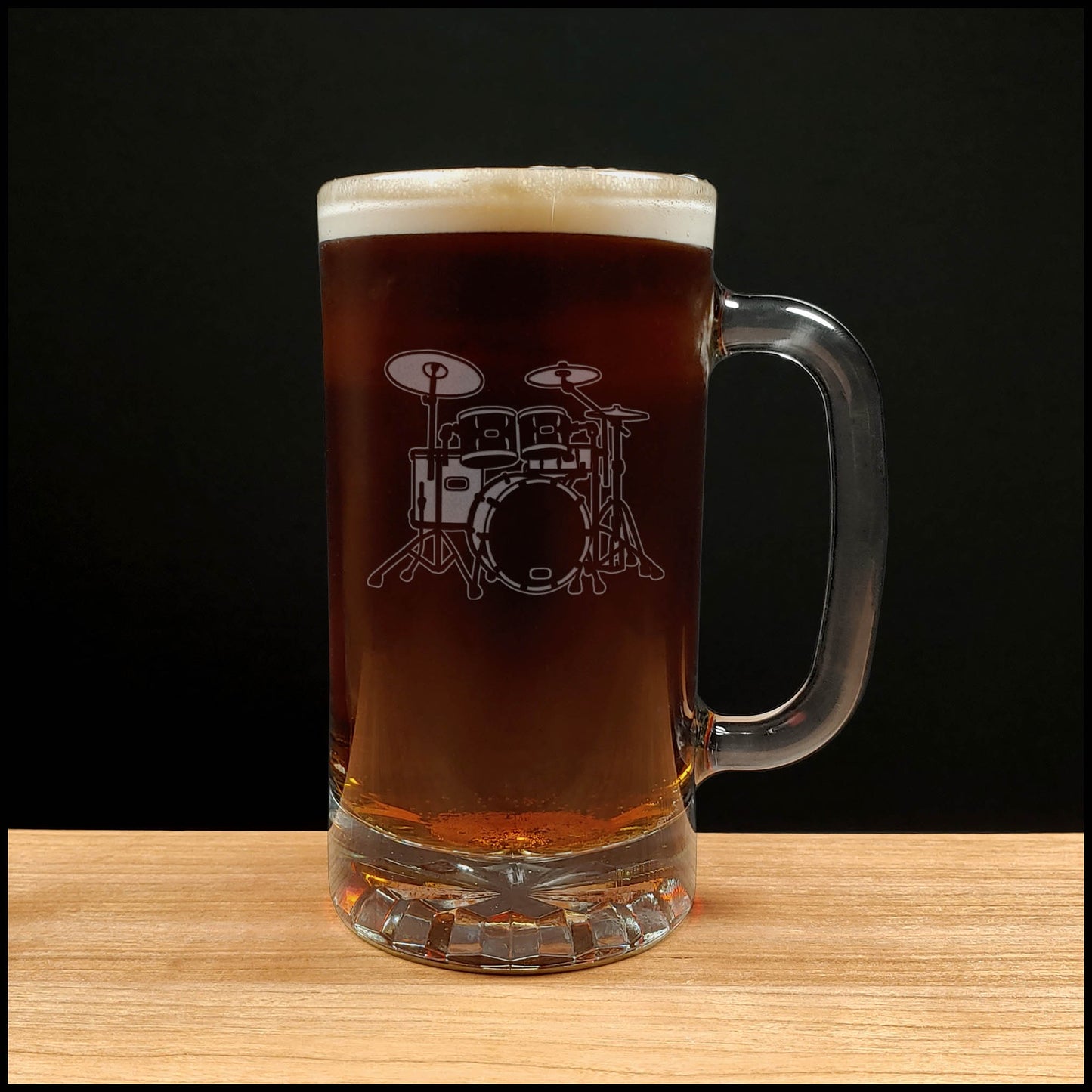 Glass mug with a drum set engraving filled with dark beer on a wooden surface 