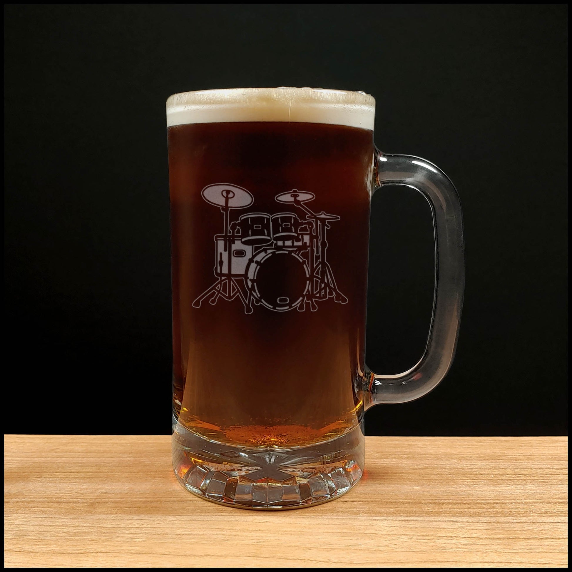 Glass mug with a drum set engraving filled with dark beer on a wooden surface 