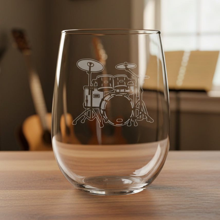 Stemless wine glass with a Drum Set etching on a wooden surface with a music room in the background