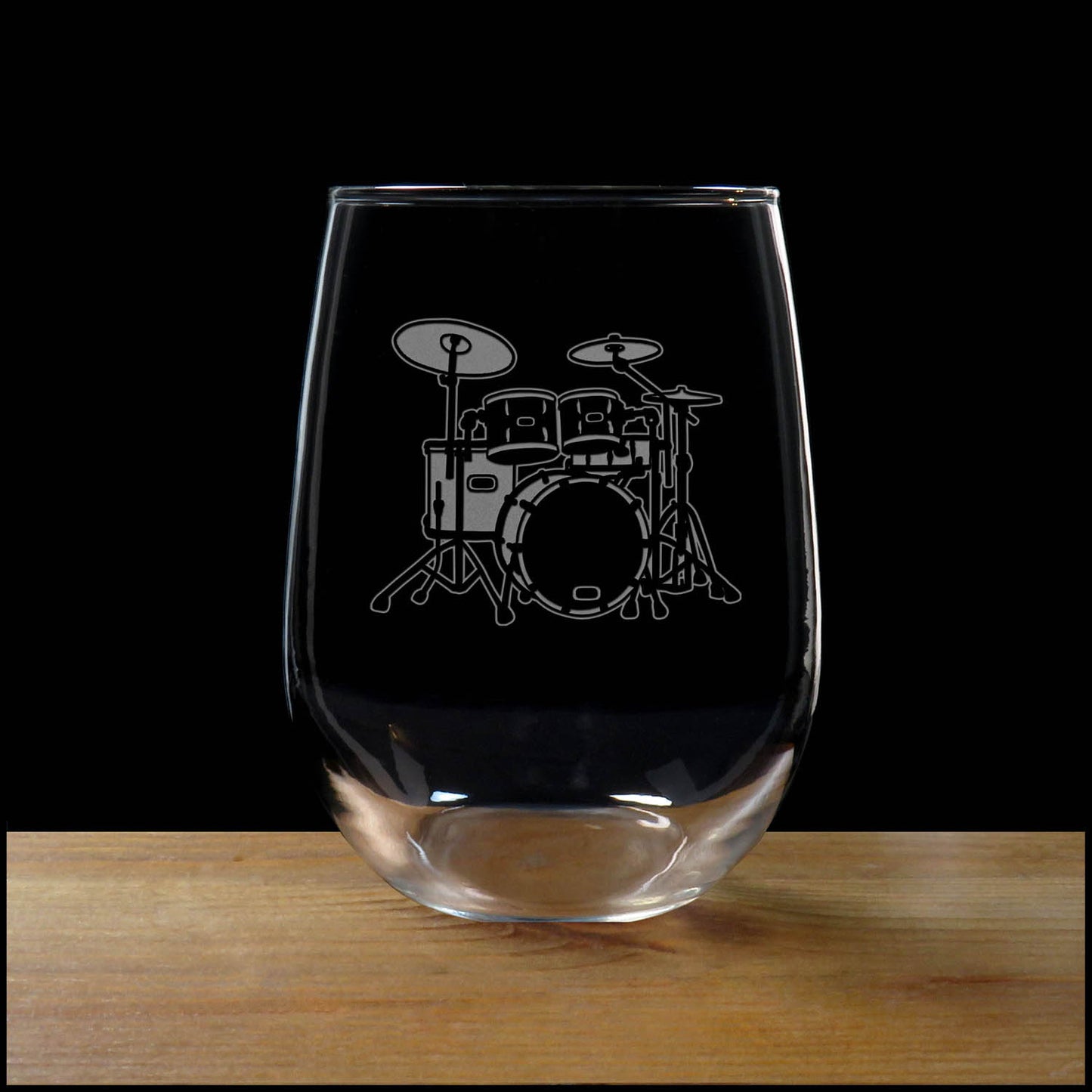 Stemless wine glass with etched Drum Set Design on a wood surface with a black background