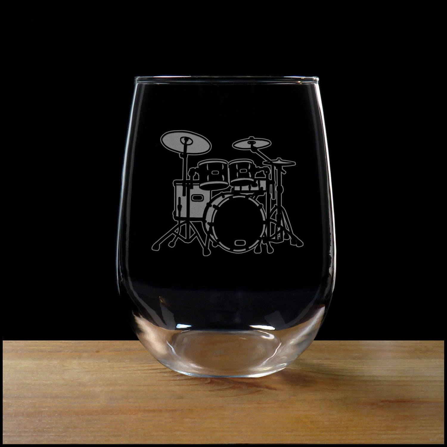 Stemless wine glass with etched Drum Set Design on a wood surface with a black background