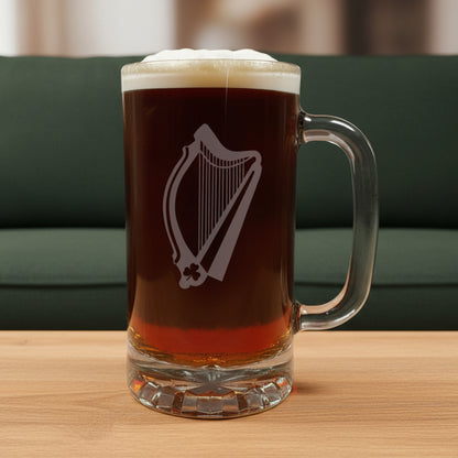 Glass mug with a harp engraving filled with dark beer on a wooden surface with a green couch in the background