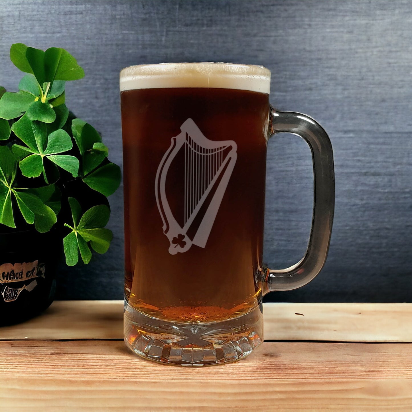 Glass mug with a harp etched filled with dark beer on a wooden surface with shamrock plant  in the background