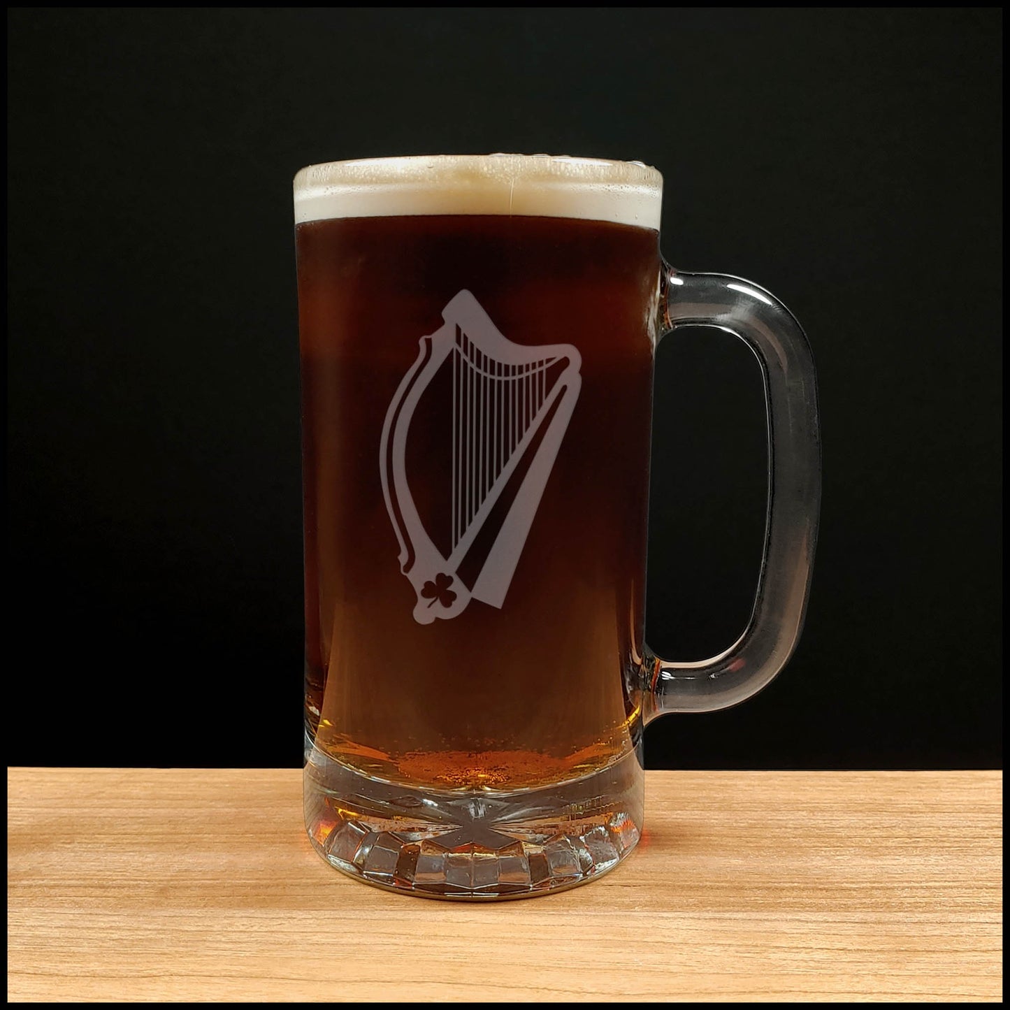 Glass mug with a harp engraving filled with dark beer on a wooden surface 