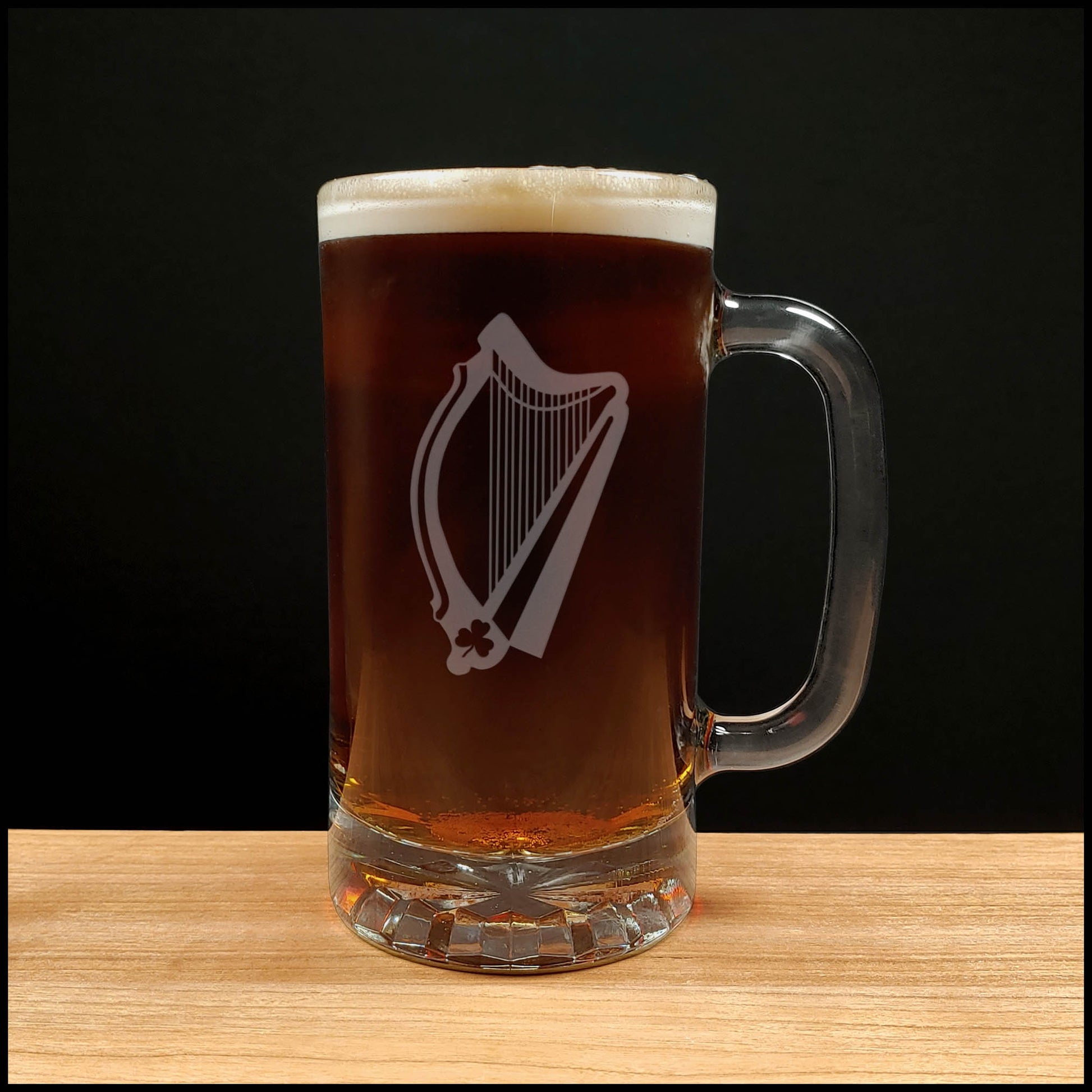 Glass mug with a harp engraving filled with dark beer on a wooden surface 