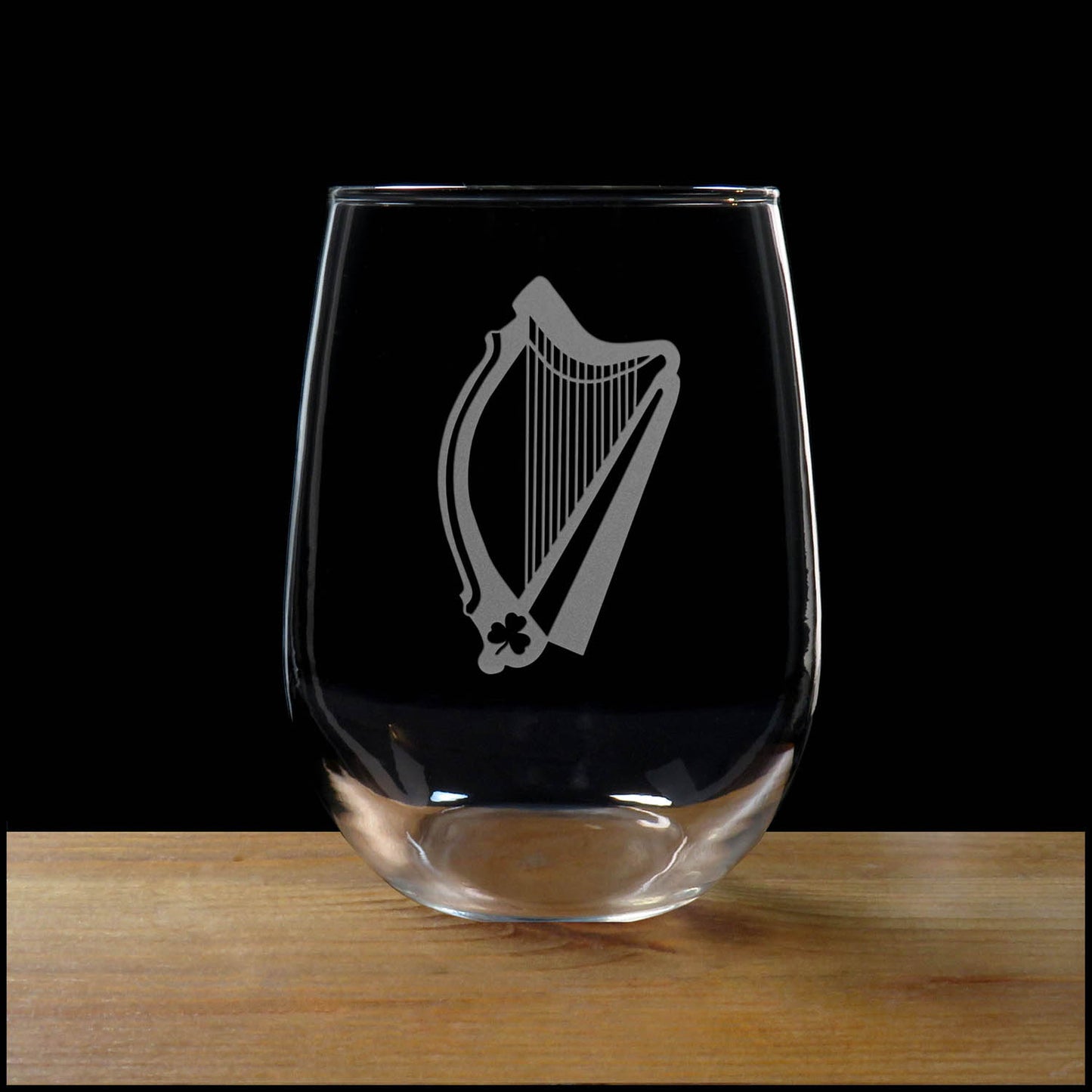 Stemless wine glass with etched Harp Design on a wood surface with a black background