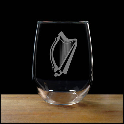Stemless wine glass with etched Harp Design on a wood surface with a black background