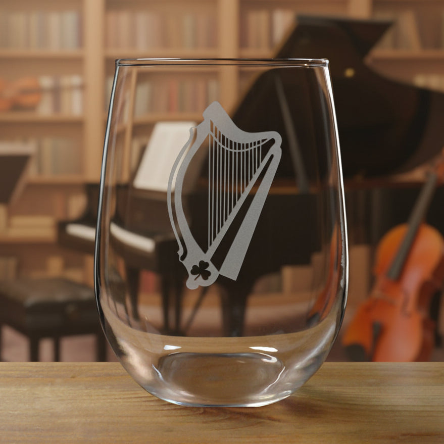 Stemless wine glass with a Harp  etching on a wooden surface with a music room in the background