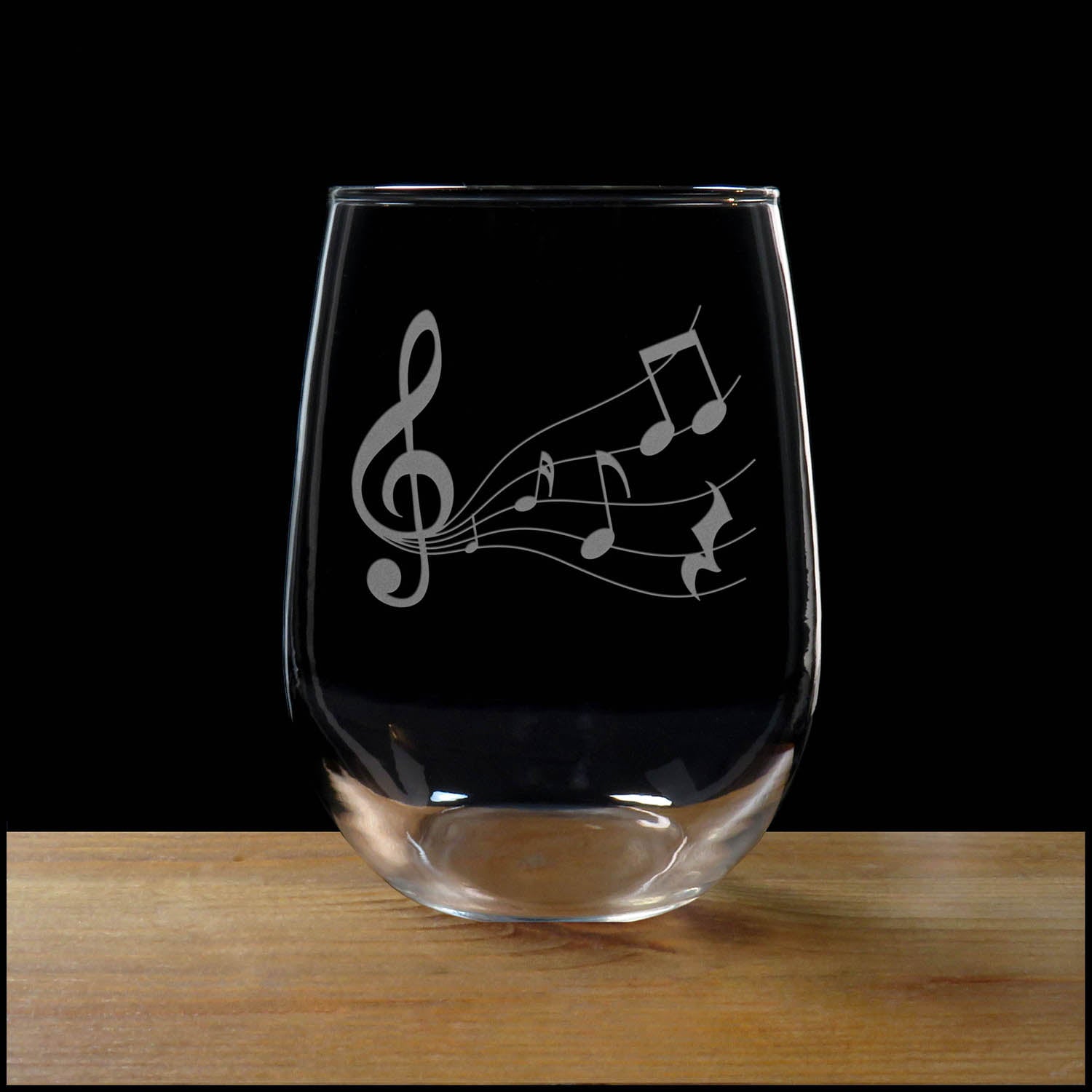 Stemless wine glass with etched Music Staff Design on a wood surface with a black background